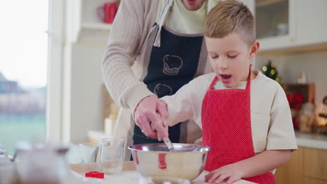 dad helps young boy mix oil and flour while baking bread