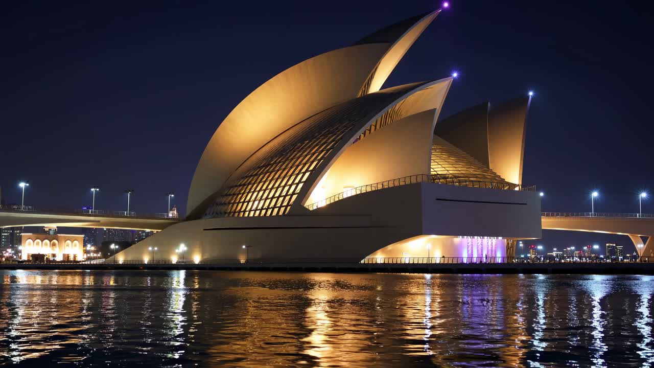 Dubai Opera glowing at night, beautifully reflecting on the water's surface, with a striking bridge in the background, creating a captivating scene in the vibrant city of Dubai, UAE
