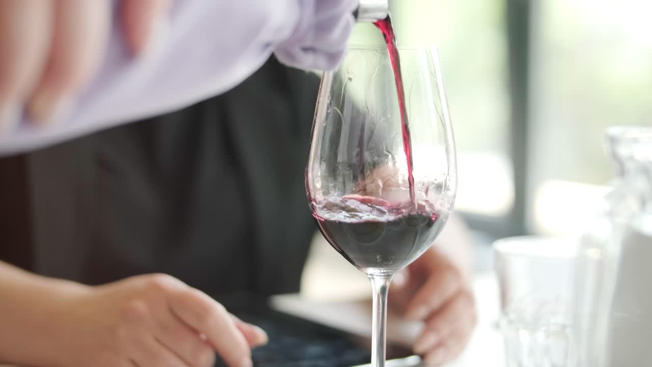 클로즈업: 익명의 웨이터 손이 술잔에 포도주를 고, 젊은 여성 손이 레스토랑 내부에서 음료와 함께 포도주 술잔을 고 있다.