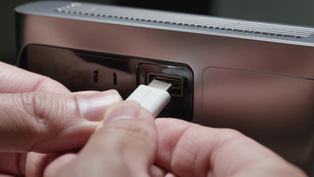 Hands inserting white USB connector as reaching to recessed port on back panel, connecting device