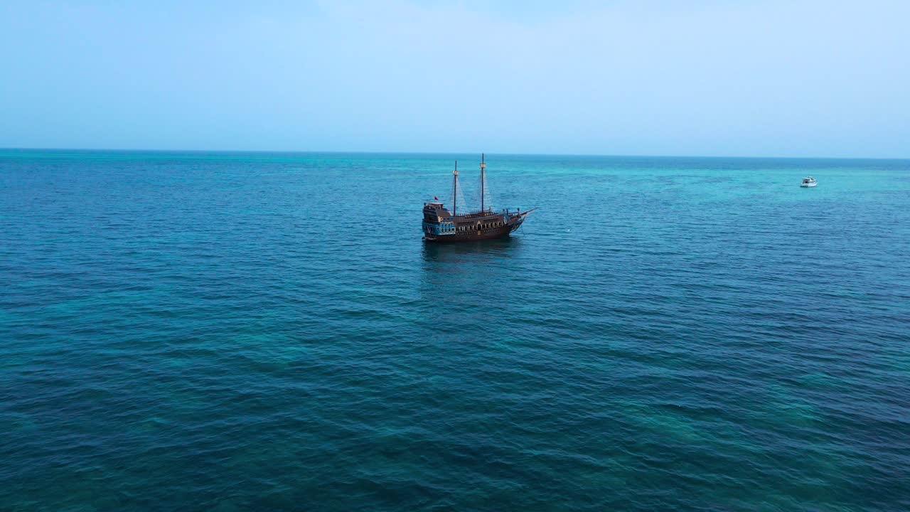A solitary sailboat drifts peacefully across the vast expanse of the ocean under a clear blue sky, evoking themes of adventure, solitude, and the endless horizon.