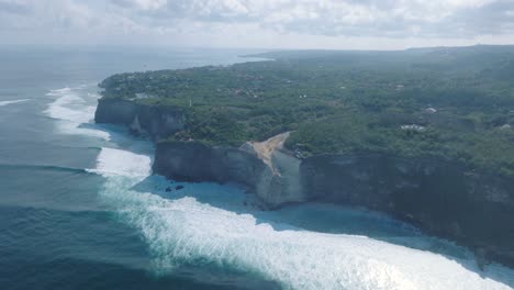 high angle drone video of environmental destruction of the limestone cliffs near pura luhur uluwatu temple, bali indonesia, with excavators, massive earth clearing, and polluted ocean