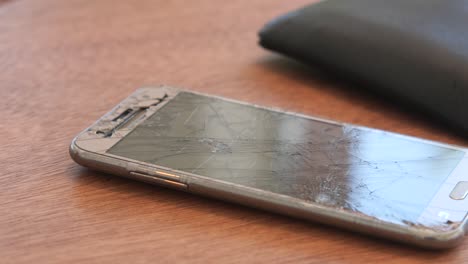 pantalla de teléfono rota y billetera en la mesa de madera