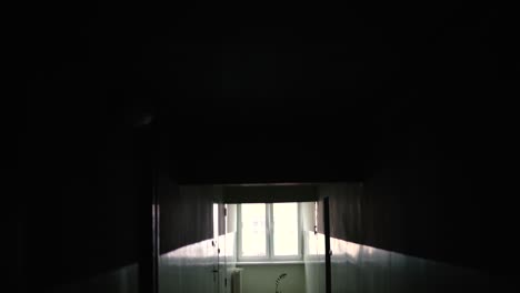 a smooth shot in an old, dark, empty corridor in a block of flats, a stylized place with a window at the end of the corridor, a view from the ceiling to the floor