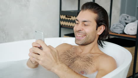 man relaxing in a bathtub with smartphone