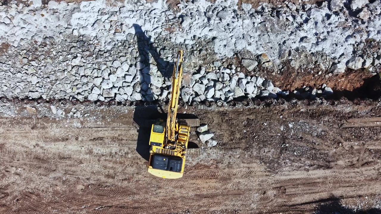 Travaux de construction sur un chantier avec de la machinerie lourde déplaçant de la terre et des roches sous la lumière de l'après-midi dans une zone dégagée avec du gravier et de la terre visibles