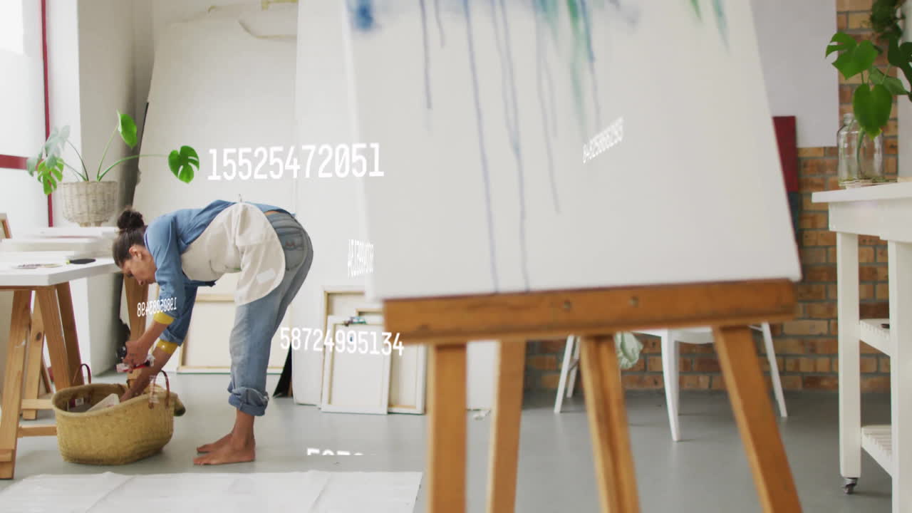 woman artist bending over art studio floor, with animated paint tubes floating around basket