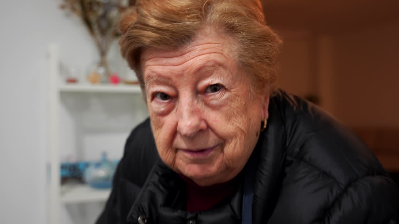 Funny grandmother gesturing and smiling, enjoying being filmed at home. Handheld