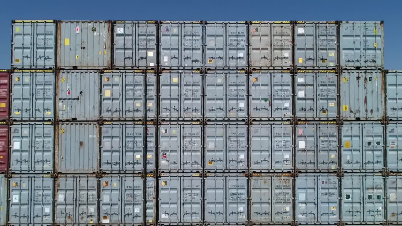Aerial view of numerous shipping containers tightly stacked in a busy shipping yard. The containers are marked with various codes, showcasing the vibrant logistics activity of the port.