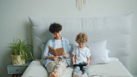 mother and son relaxing in bedroom reading and using tablet