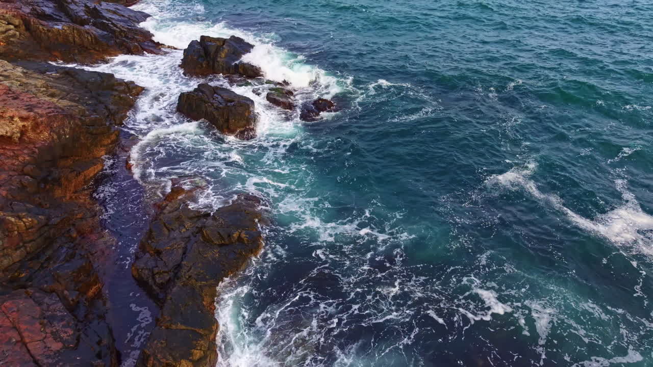 Waves crash against rugged coastal rocks at sunset, highlighting nature's beauty and power in this serene seaside view