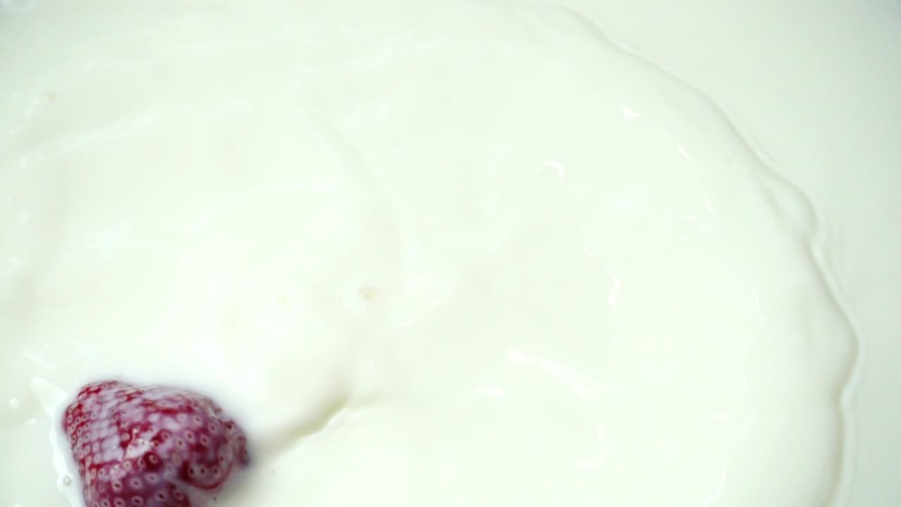 Berries of strawberry fall in milk. Slow motion. Shooting of strawberry