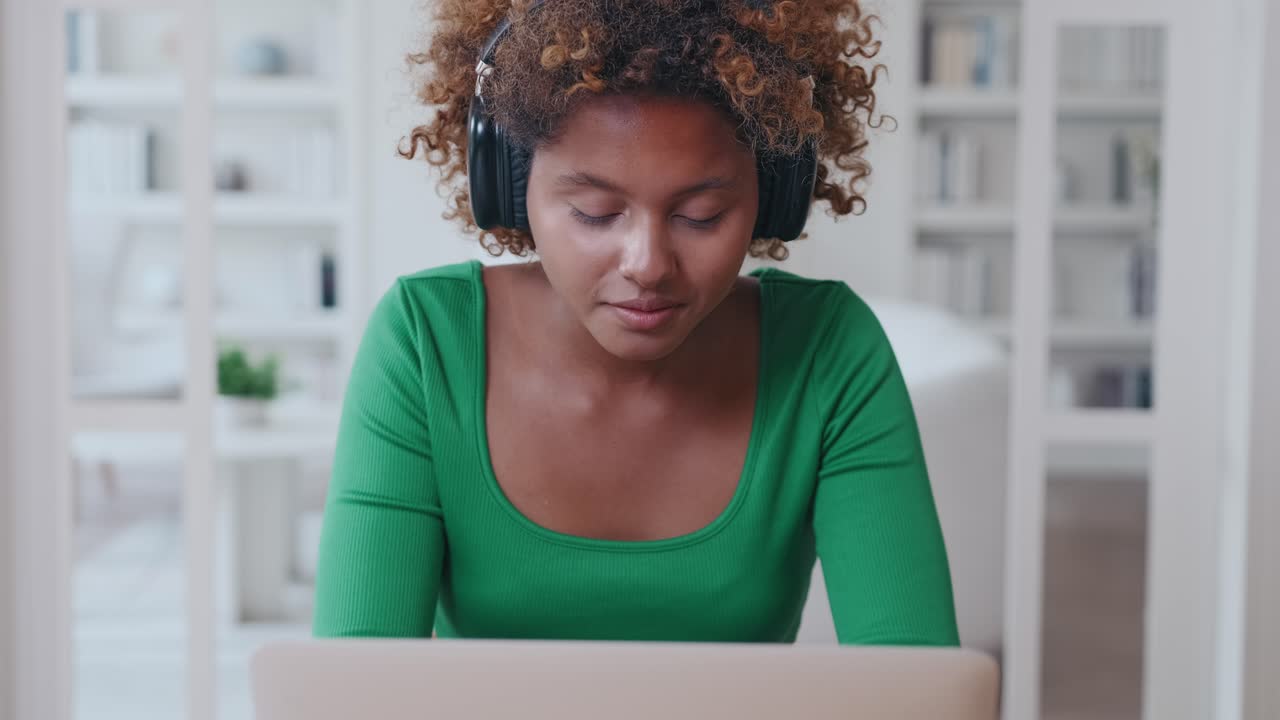 Junge, entspannte, afroamerikanische Frau mit Kopfhörern arbeitet online als Buchhalterin
