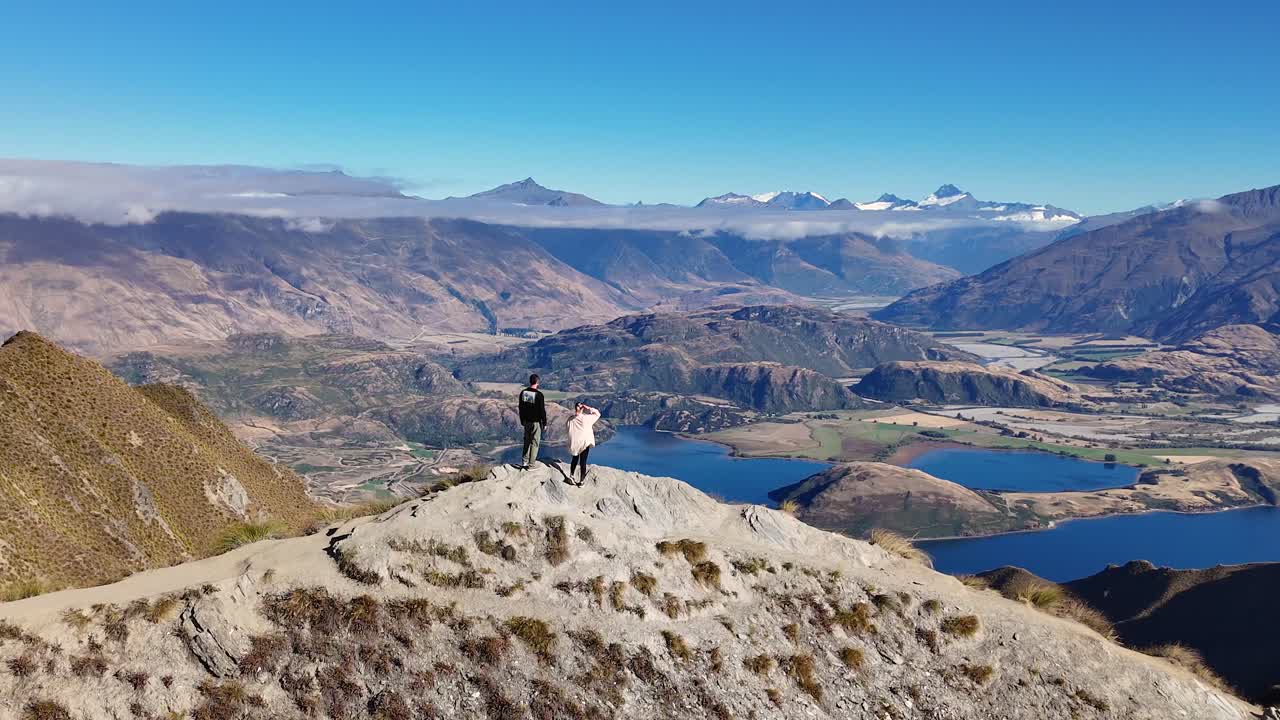 A 4K drone circles a couple at the famous Roy’s Peak viewpoint in Wanaka, New Zealand. Towering mountains, alpine trails, and turquoise lakes create a breathtaking South Island scene