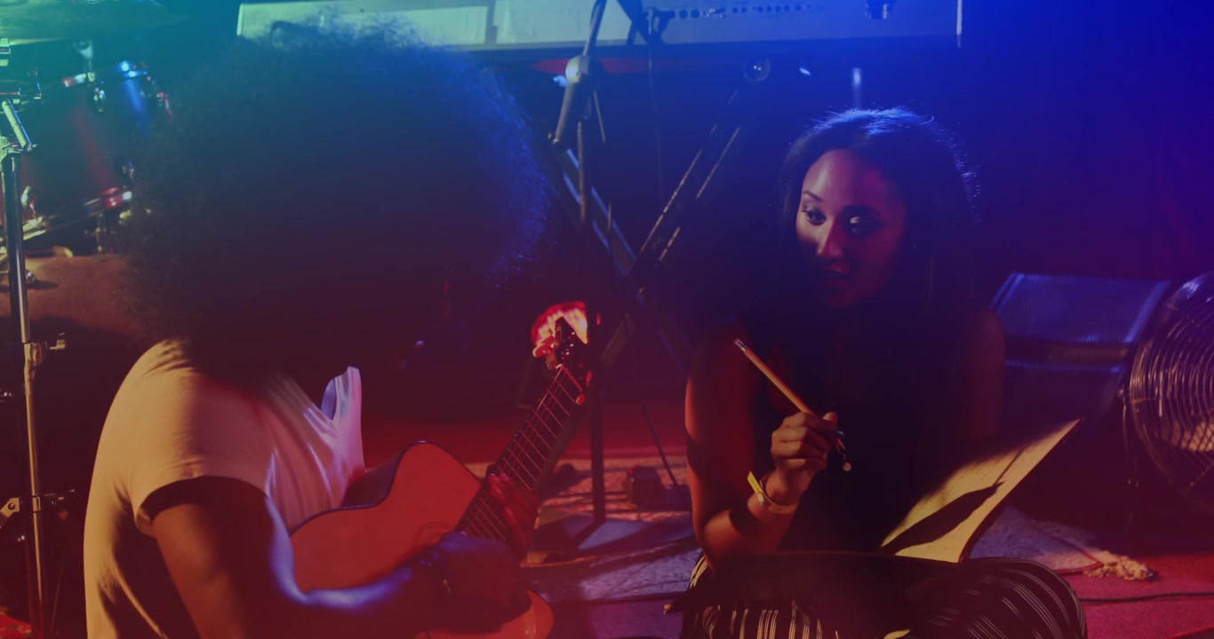 Animation of glowing red and blue lights over african american man playing guitar and woman writing
