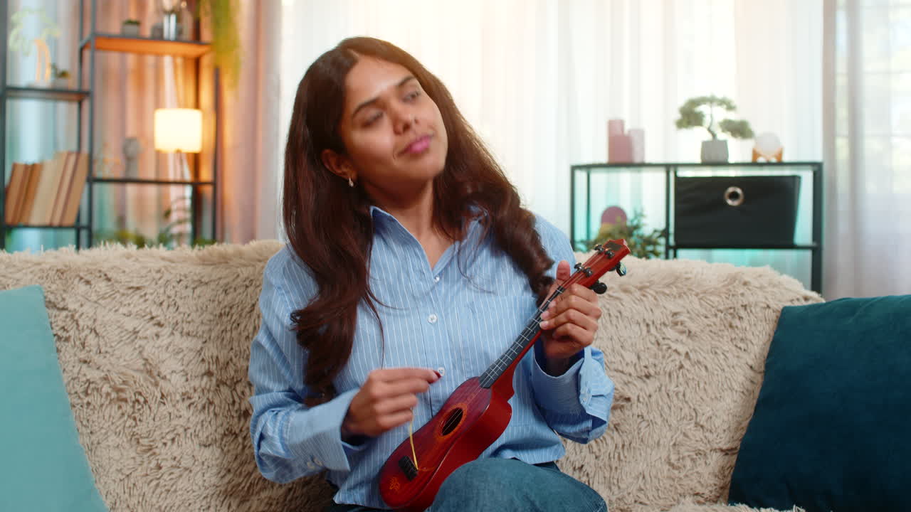 Indian woman playing toy ukulele with joyful emotion laughing and pretending to perform at home