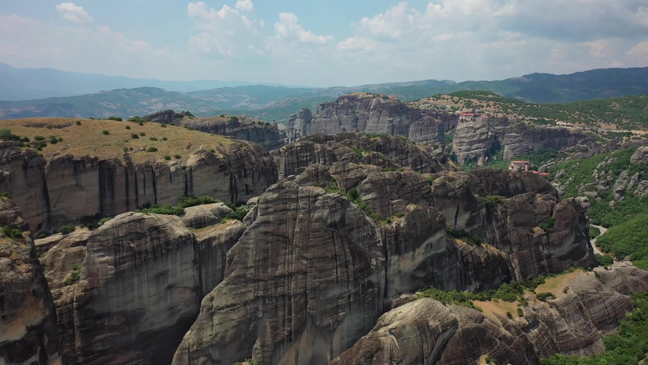 Meteora'nın kaya sütunlarının ve kayalıklara tünemiş antik manastırların büyüleyici drone panoraması. Görüntüler, geniş taş ormanını, yemyeşil vadileri ve aşağıda yer alan Kalabaka kasabasını gösteriyor.