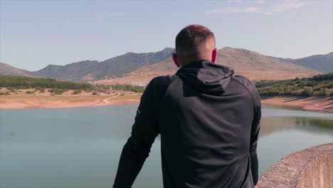 Man-standing-on-a-dam-of-a-lake-sightseeing-the-beautiful-nature