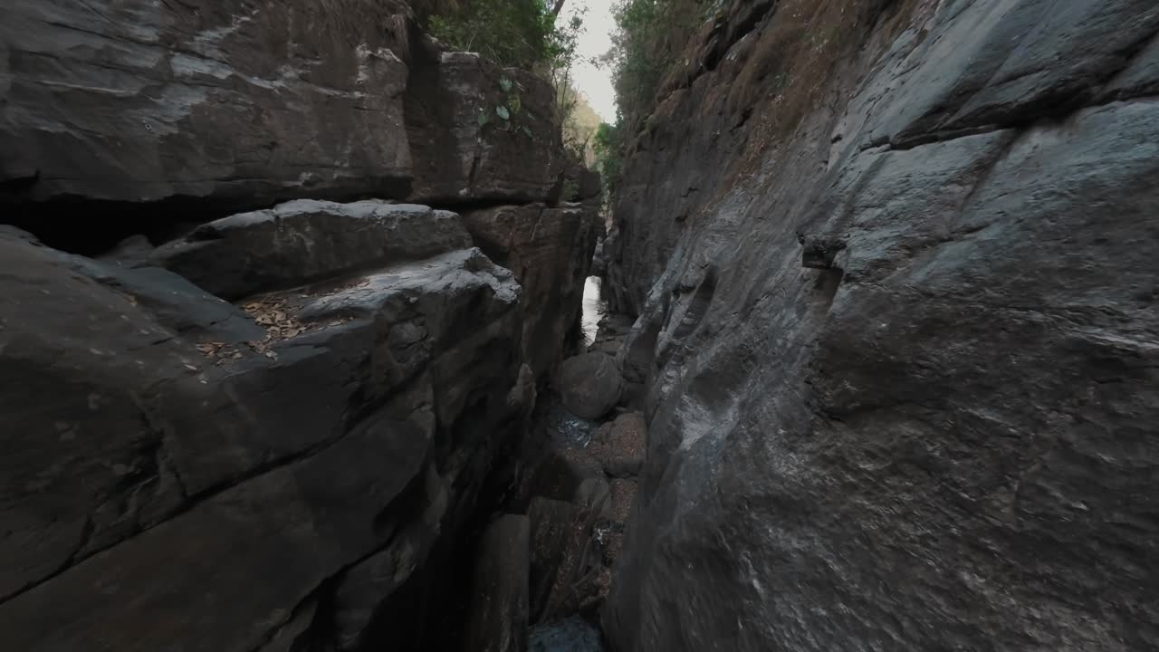 FPV flying smoothly through the deep and narrow Kenios Raizama canyon in Chapada dos Veadeiros, Brazil, showcasing the powerful Sao Miguel River cutting through ancient rock walls