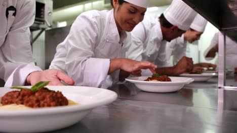 Row-of-chefs-garnishing-spaghetti-dishes