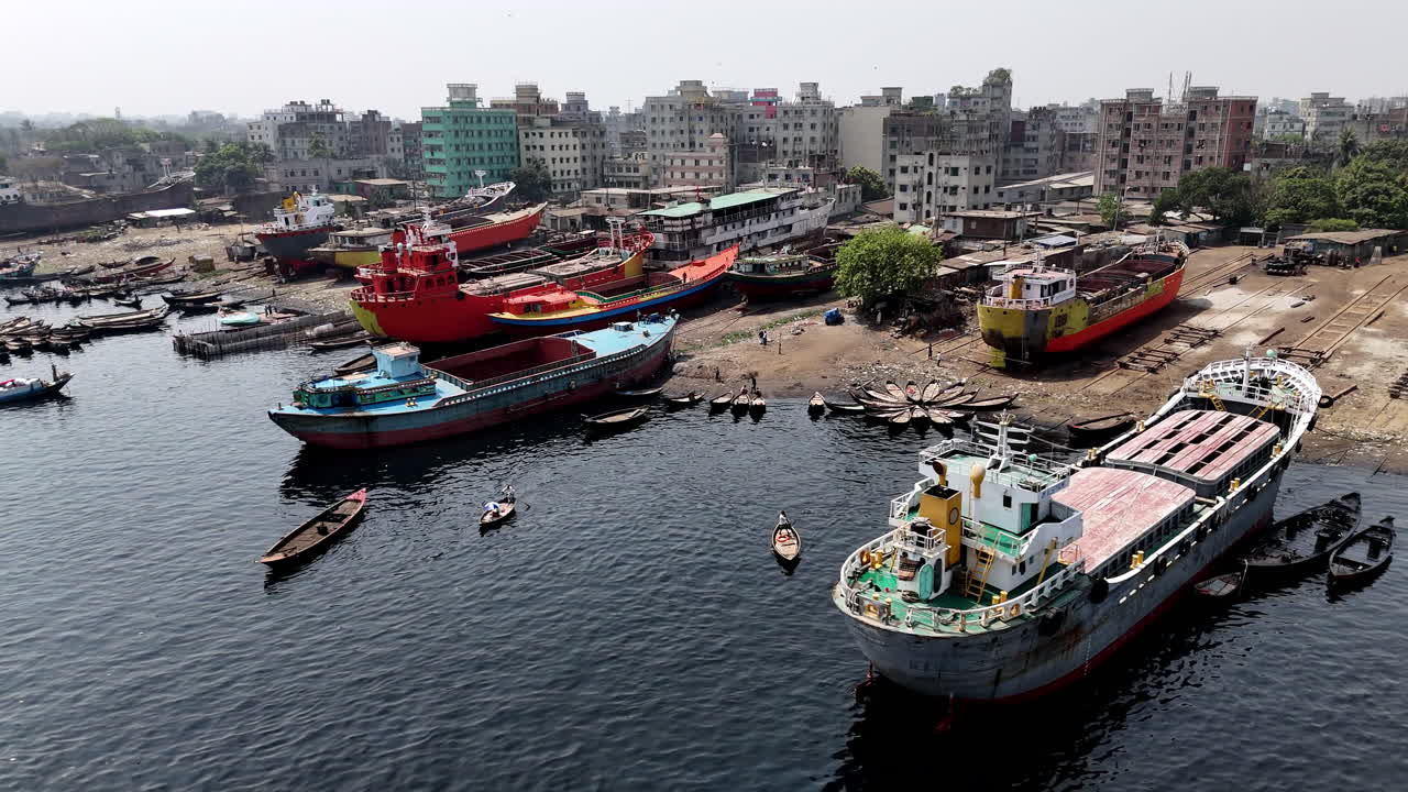 Cinematic slow pan aerial shot showing large cargo ships docked along the shore of the Buriganga river in Dhaka, Bangladesh