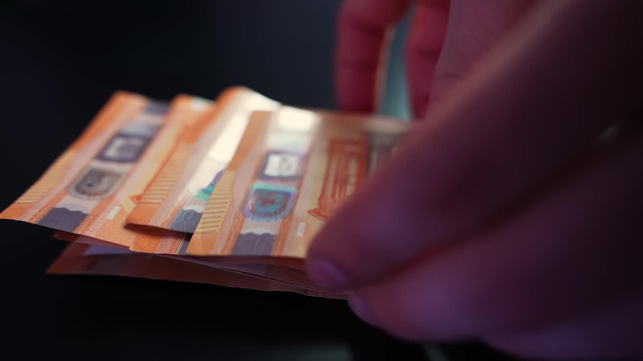 En hånd lægger 50-eurosedler på et mørkt bord i nærbillede, der viser kontant betaling, budgettering, opsparing og forretningsfinansielle koncepter med plads til tekst.