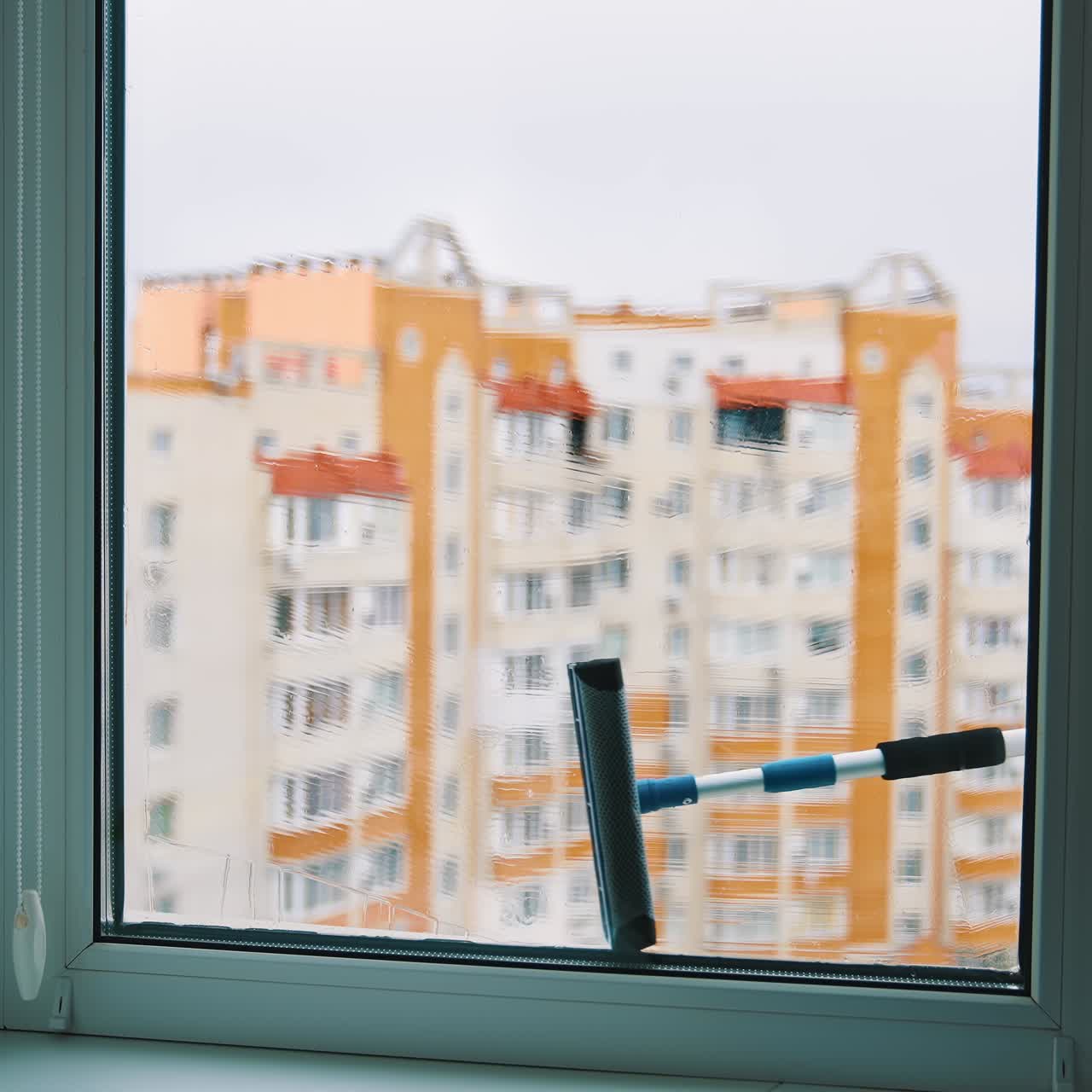 Plastic window is washing with brush. Window cleaning brush washes glass window from outside on high-rise building background
