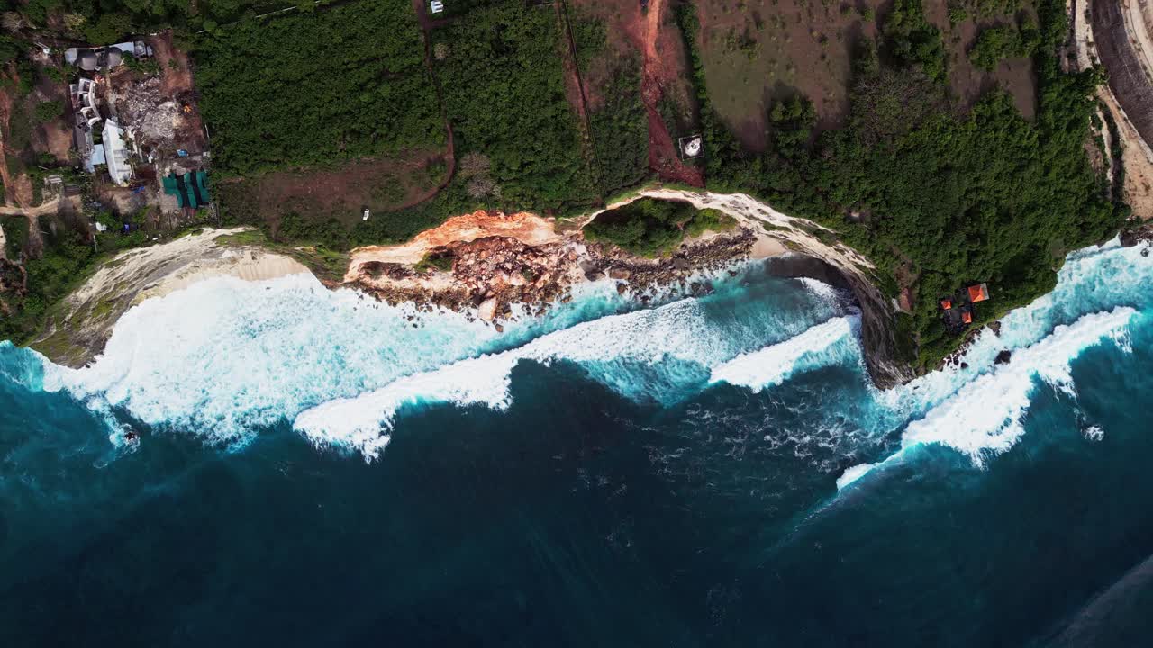 Drone video showing Bali coastline from above with breaking ocean waves moving over deep blue water and rugged natural cliff creating a clear tropical seascape with detailed shoreline