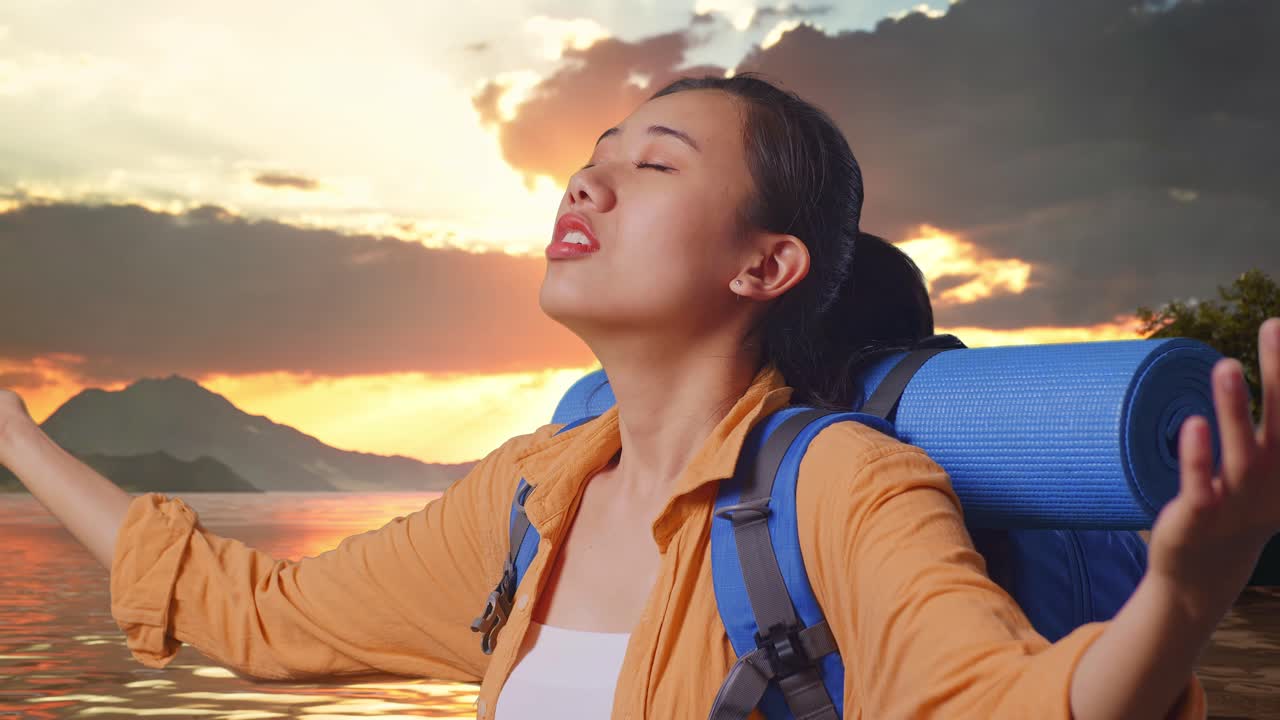 Close Up Side View Of Asian Female Hiker With Mountaineering Backpack Spreading Arms Enjoy Looking The View Around While Standing At A Lake During Sunset Time