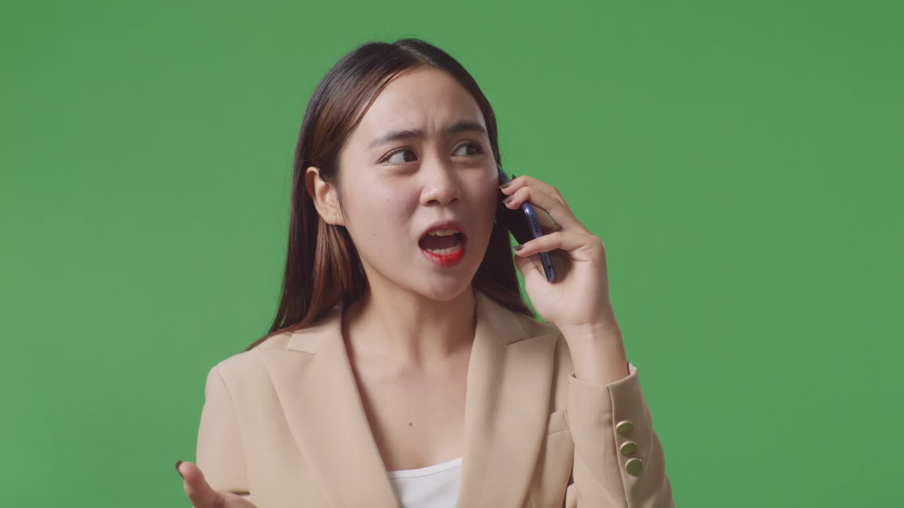 화가 난 아시아 사업가 여성이 스튜디오에서 녹색 화면에 서서 휴대 전화로 이야기하고 있습니다.