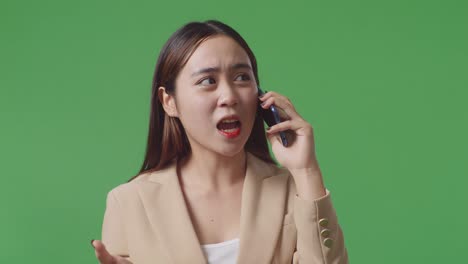 화가 난 아시아 사업가 여성이 스튜디오에서 녹색 화면에 서서 휴대 전화로 이야기하고 있습니다.