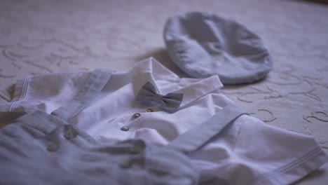 adorable baby boy outfit with bow tie, suspenders, and matching cap laid out on a lace covered surface, perfect for a special occasion like baptism