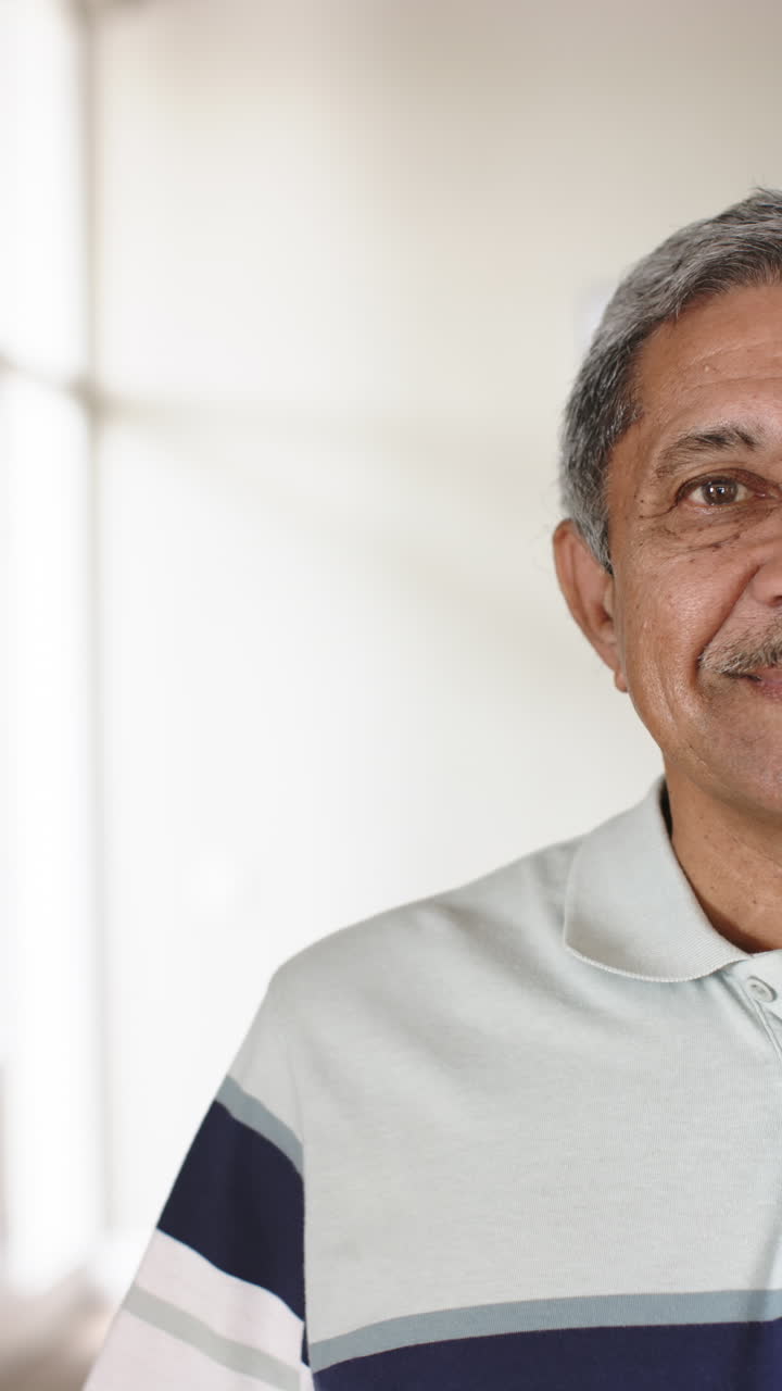 Vertical video of half portrait of happy biracial senior man at home, slow motion