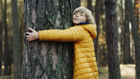 Side-view-of-a-cute-little-teen-boy-hugging-a-tree-trunk-with-eyes-closed-in-the-forest