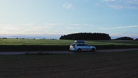 silver suv driving on a rural road through fields at sunset