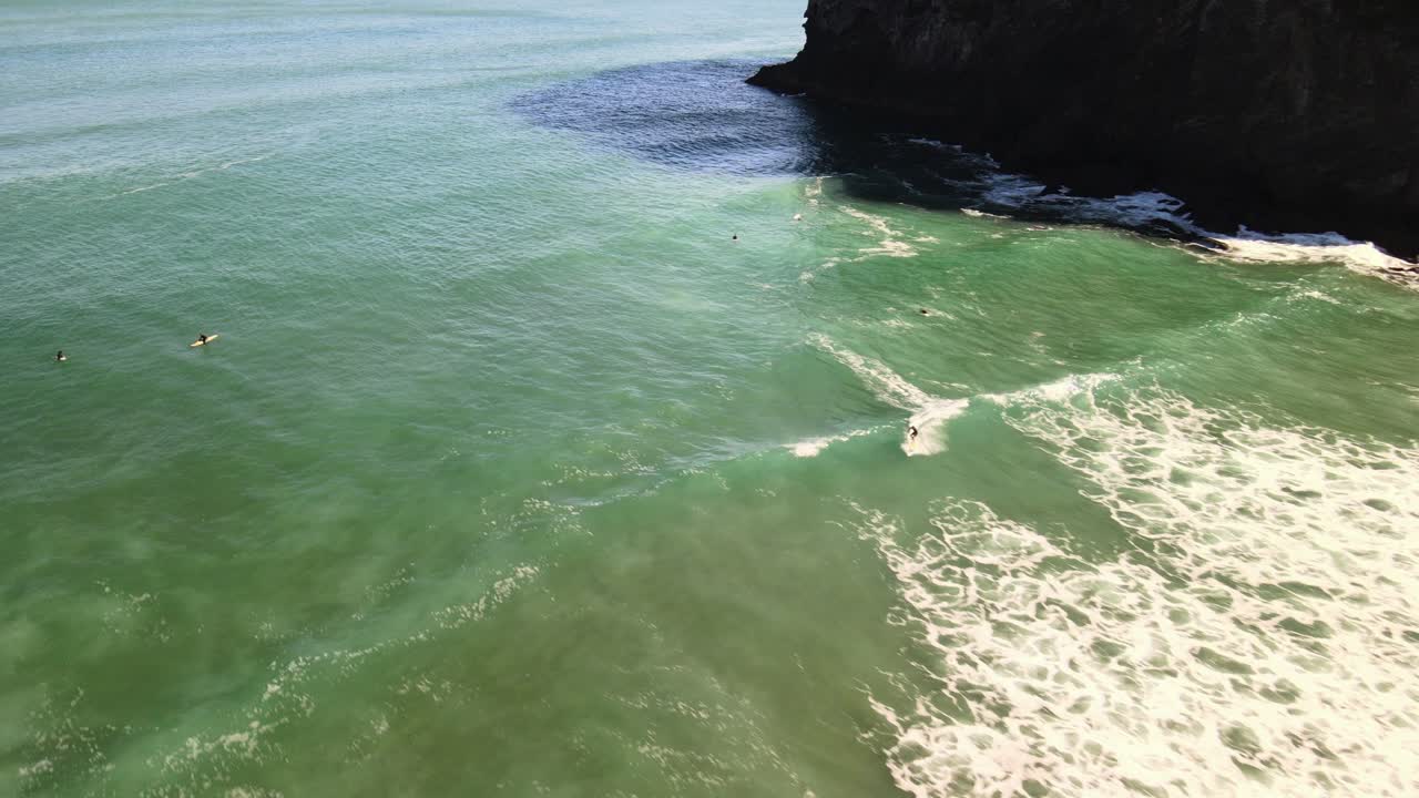 video aéreo de un surfista montando un descanso con la mano derecha en la playa de arena negra de piha en nueva zelanda