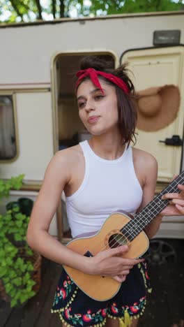 young woman playing ukulele by campervan