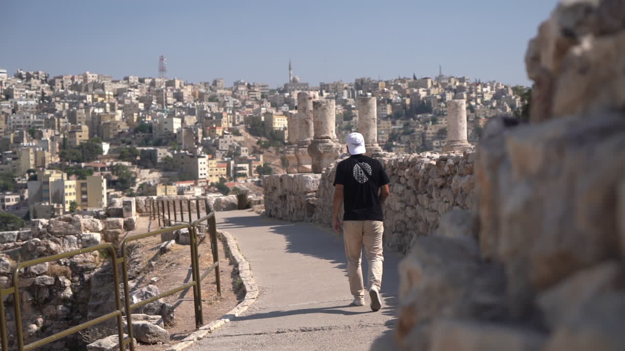 hombre caminando por las paredes de la antigua ciudadela de amman, jordania con ruinas y paisaje urbano en segundo plano, cámara lenta, cuadro completo