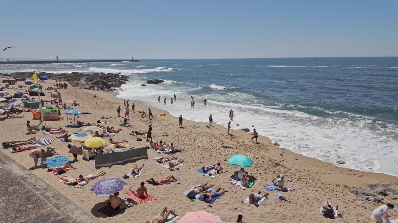 People enjoy a sunny day on Porto's Ingleses beach, relaxing and swimming by the ocean