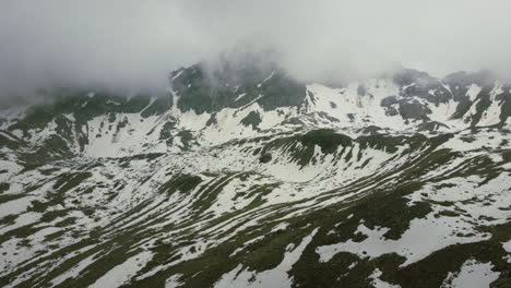 Overcast-winter-day-in-Zernez-Switzerland-with-clouds-rolling-over-mountain-peaks-covered-in-snow,-aerial-dolly-zoom