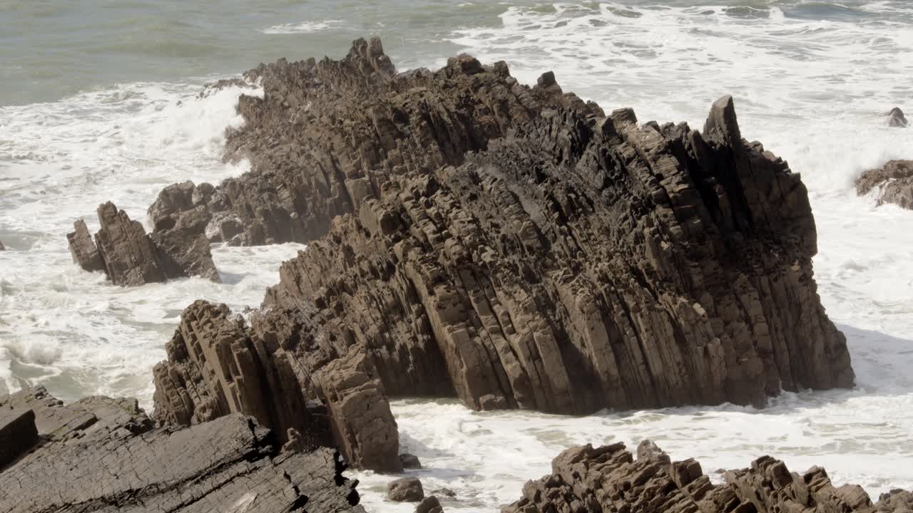 medio disparo de olas chocando contra rocas sedimentarias dentadas en el mar de cornualles en el muelle de hartland, stoke, hartland, bideford