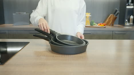 woman displaying a set of pots and pans in a kitchen.