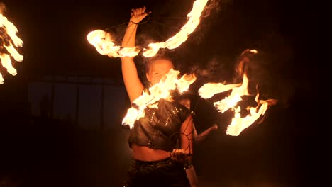 tres mujeres con aros ardientes bailan con antorchas ardientes en ropa de cuero en un hangar oscuro demostrando un espectáculo de fuego de circo en cámara lenta.