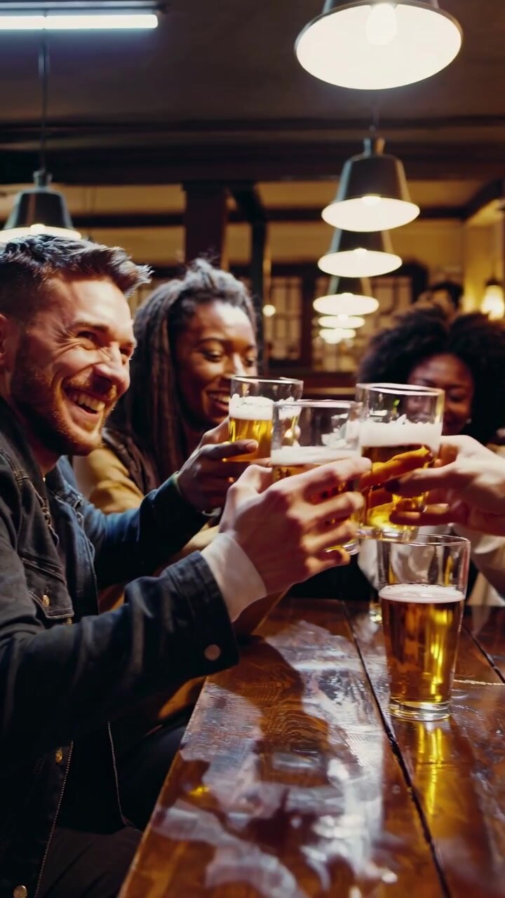 Gruppo eterogeneo di amici che brindano con birra in un pub