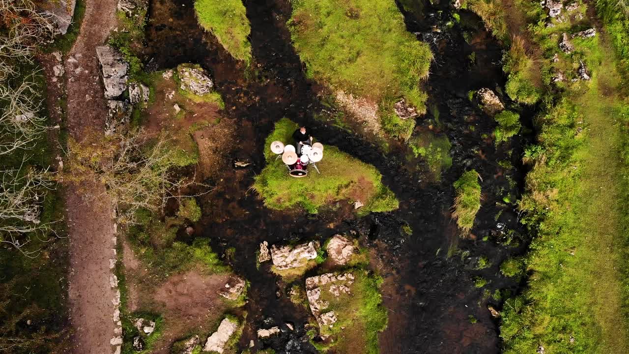 dron descendiendo sobre el baterista tocando solo en una pequeña isla en la corriente