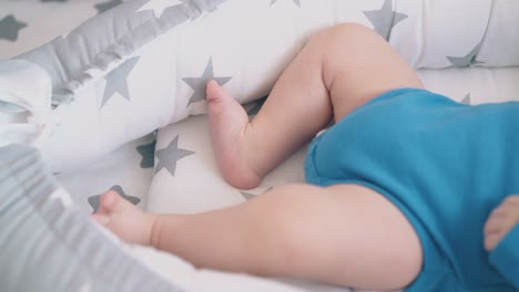 little-boy-in-bodysuit-kicks-funny-legs-in-cocoon-closeup