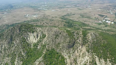 Disparo-De-Un-Dron-Que-Se-Aleja-Lentamente-De-La-Montaña-Y-Muestra-El-Resto-De-Los-Diferentes-Accidentes-Geográficos-Circundantes,-Como-Los-Campos-Y-Llanuras-De-La-Cercana-Ciudad-De-Rupite-En-Petrich,-Bulgaria.