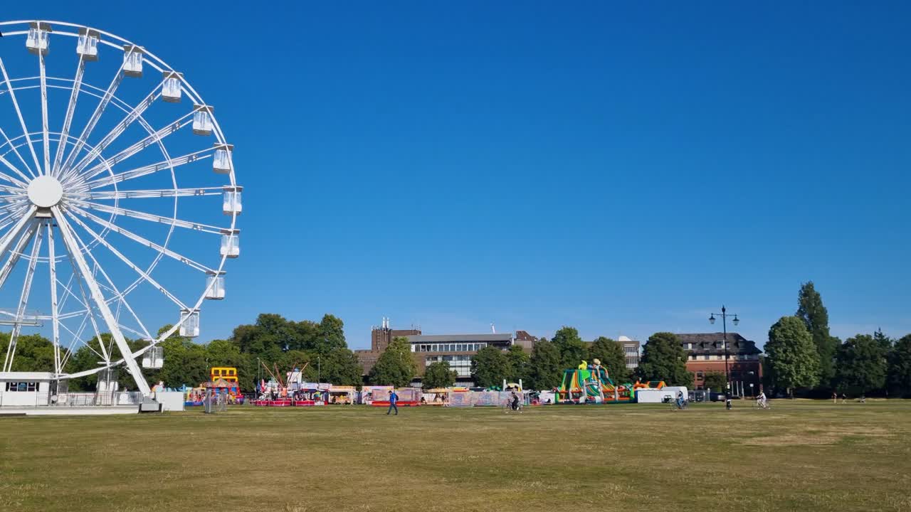 White City View Wheel slowly turns on Parker’s Piece in Cambridge, UK, under a bright blue sky, with the surrounding park and cityscape in view