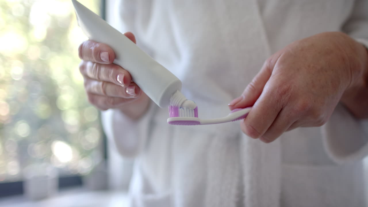 A mature Caucasian woman is putting toothpaste on brush