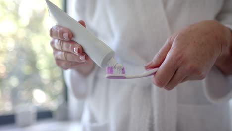 a mature caucasian woman is putting toothpaste on brush